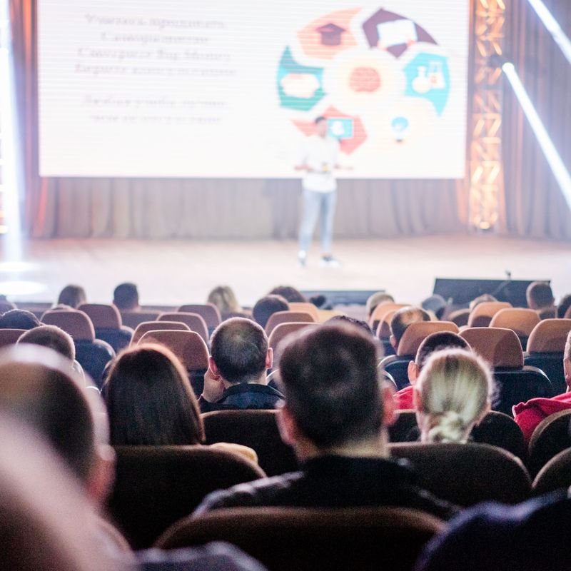 A conference audience facing a speaker on stage