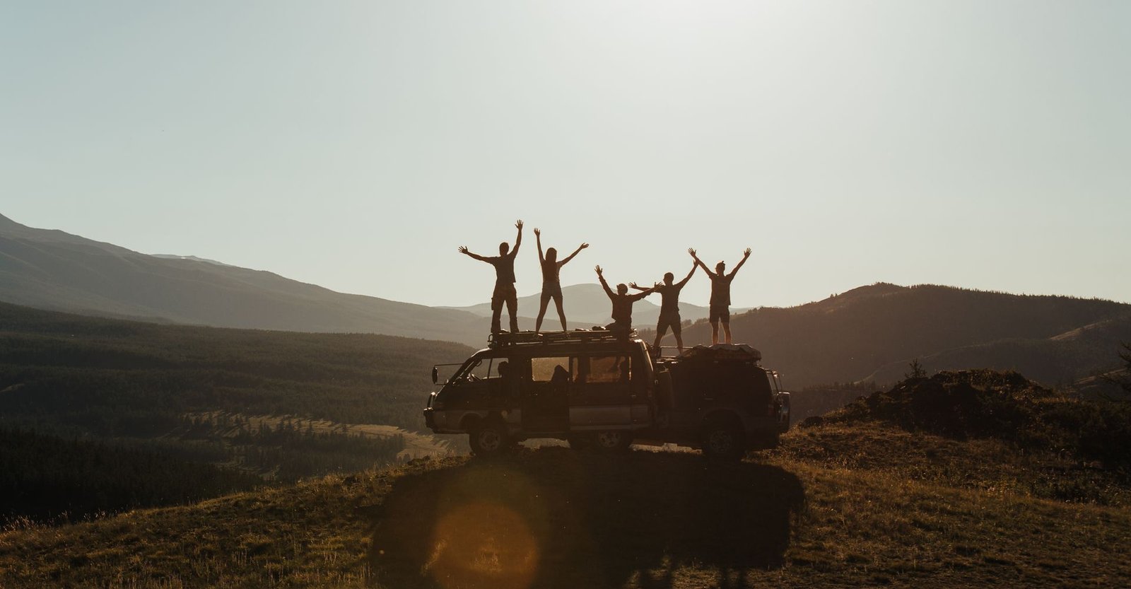 Travellers with their arms raised on top of a van at sunset