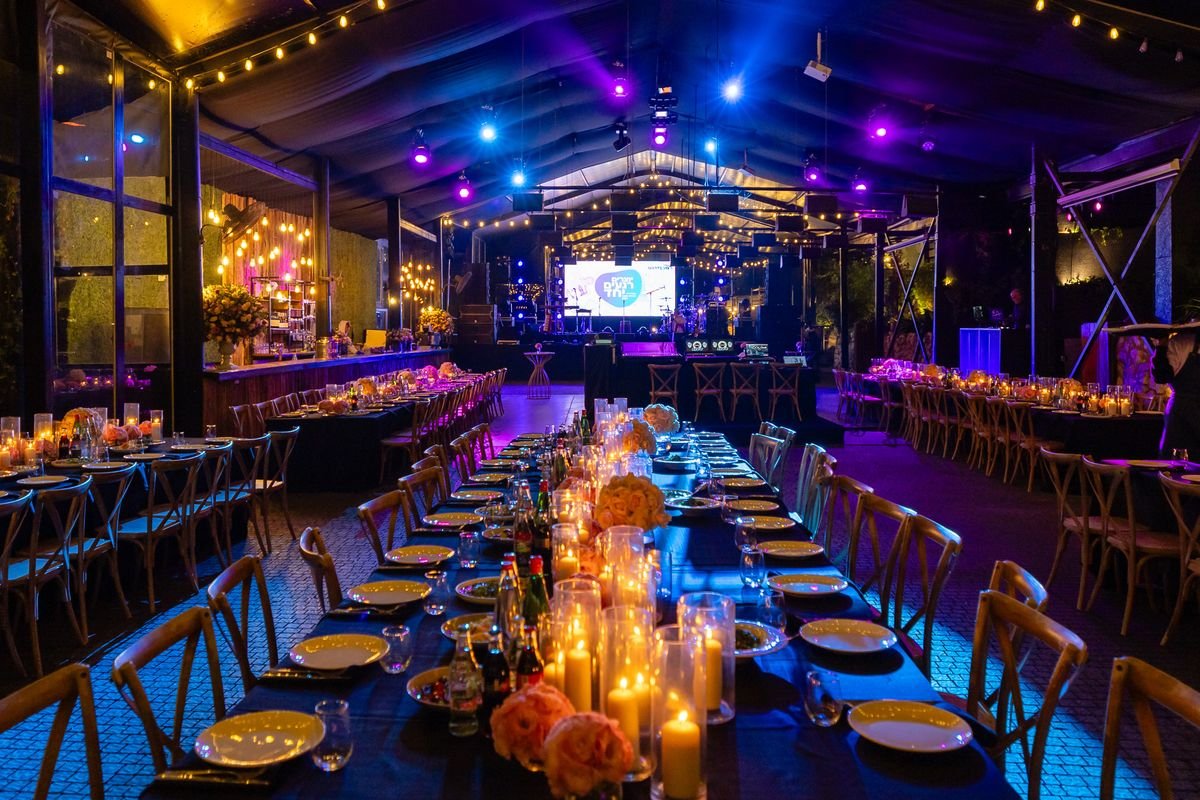 An evening venue with candle-lit long tables set in front of a lit stage