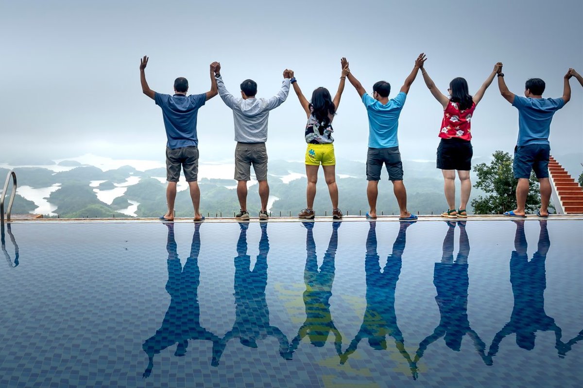 A group standing hand in hand at the edge of a hilltop infinity pool